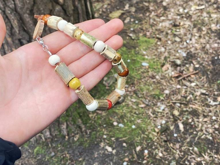 In einer geöffneten Hand liegt ein Armband aus zum Beispiel Holzteilen.