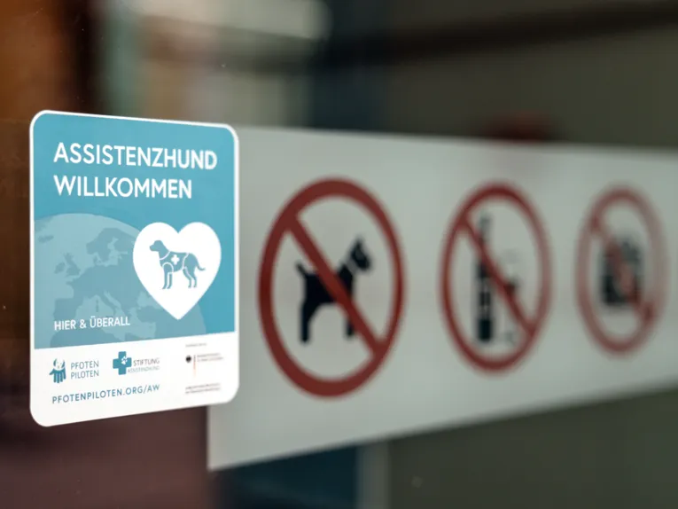 Aufkleber mit der Aufschrift "Assistenzhund Willkommen" an einer Eingangst&uuml;r.