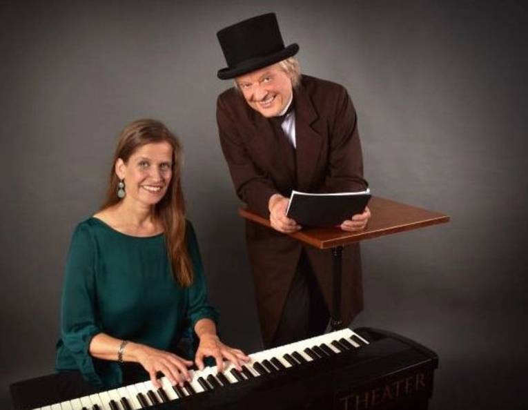 Eine Frau mit langem Haar an einem Klavier und ein Mann in Frack und Zylinder mit einem Manuskript an einem Stehpult