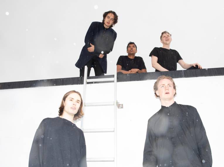 Fünf Männer, zwei stehen vor einer Mauer mit Leiter, drei oben hinter der Mauer.