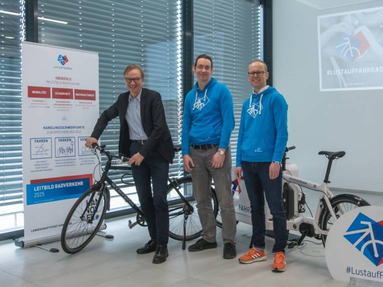 Drei Männer mit einem Fahrrad in einem Saal.