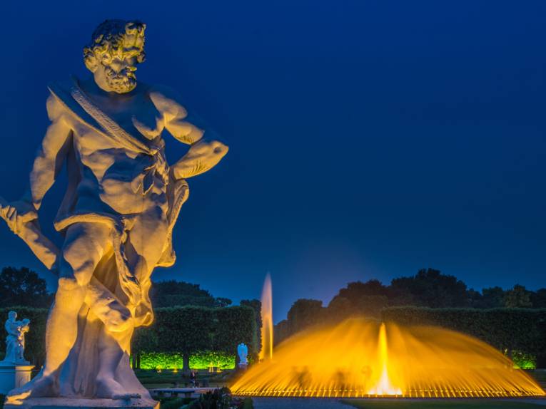 Beleuchtete Statue und Springbrunnen im abendlichen Großen Garten