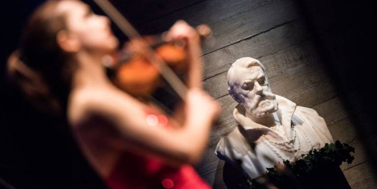 Büste eines Mannes mit unscharf aufgenommener Geigerin im Vordergrund