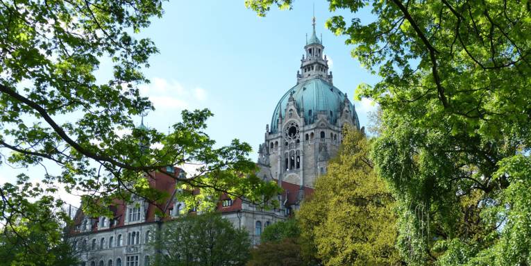 Das Neue Rathaus Hannover, eingerahmt von grünen Bäumen.