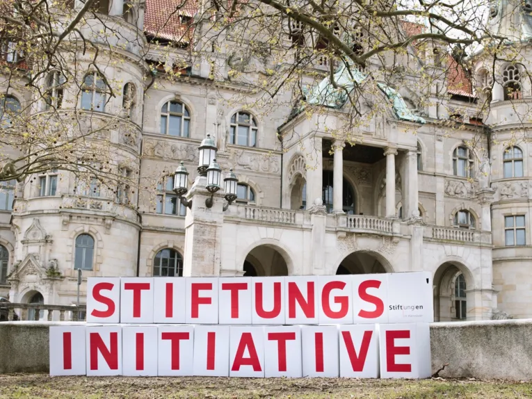 Kartons mit Buchstaben, die das Wort Stiftungsinitiative ergeben, vor einem historischen Gebäude