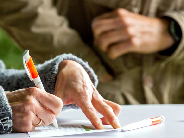 Jemand unterschreibt etwas, daneben steht eine weitere Person.