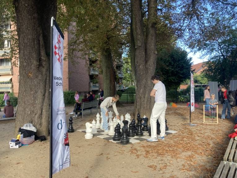 Auf einem gro&szlig;en Schachfeld spielen junge Menschen Schach