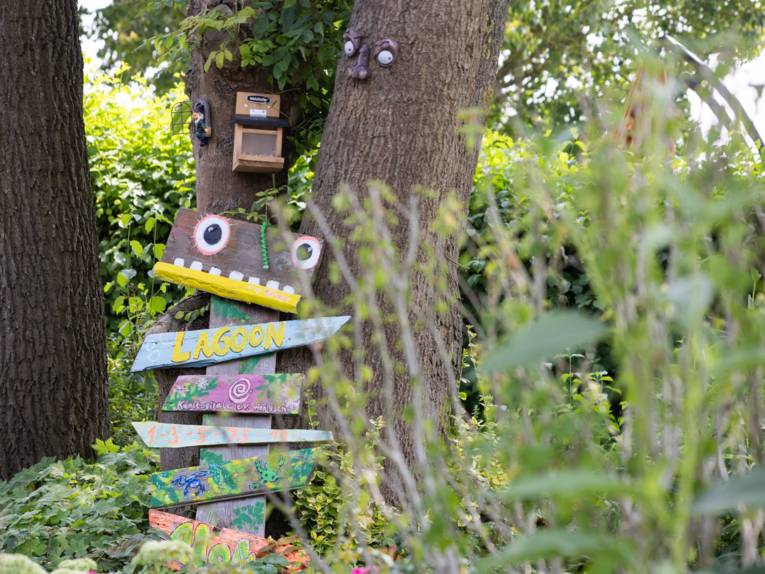 Auf Holz gemalte Wegweiser zu unterschiedlichen Orten im Freibad