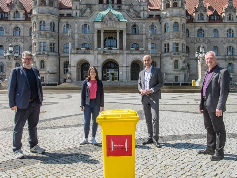 Vier Personen stehen um eine gelbe Wahlurne herum auf dem Trammplatz vor dem Neuen Rathaus