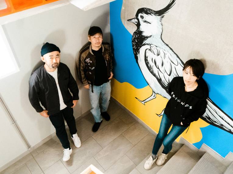 Drei Personen stehen in einem Treppenhaus und wurden von einem erhöhten Standpunkt aus fotografiert.