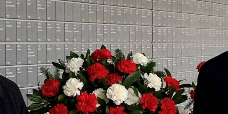 Blumen zwischen Schultern vor der Wand der Namen.