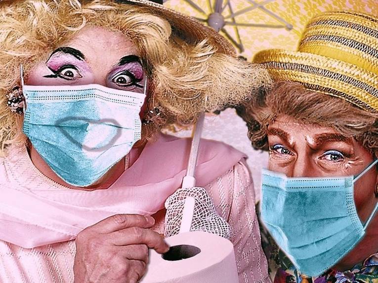 Zwei grell geschminkte und verkleidete "Damen" mit Mundschutz