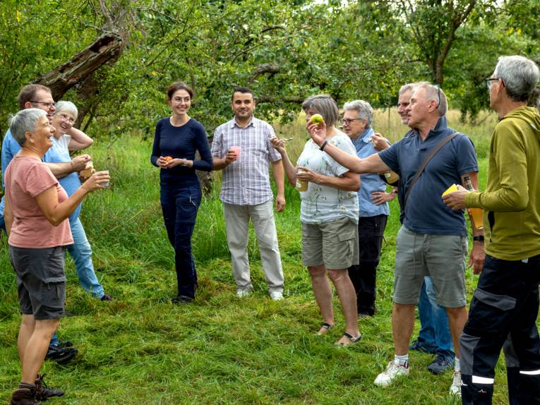 Personen stehen mit Apfelprodukten auf einer Wiese.