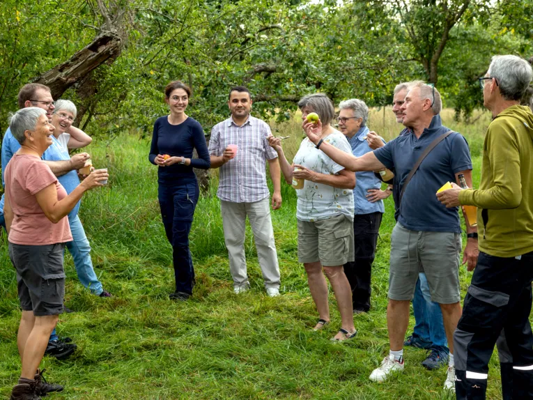 Personen stehen mit Apfelprodukten auf einer Wiese.