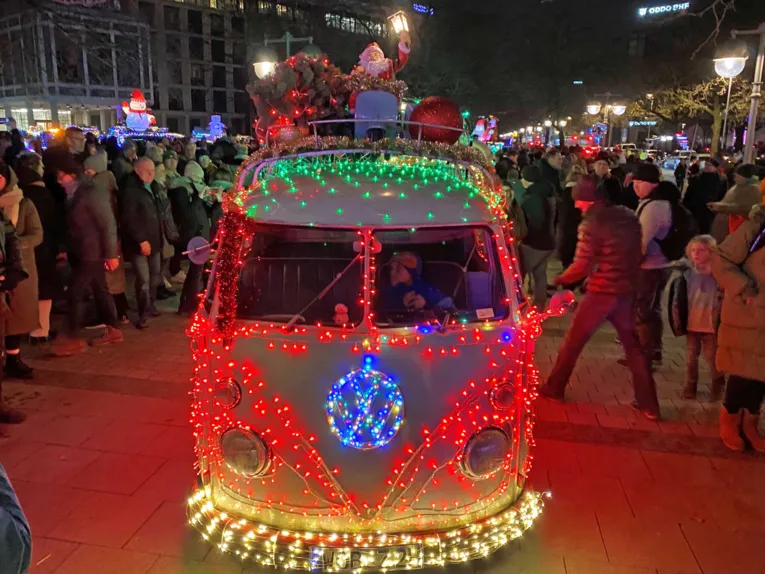 Mit Weihnachtslichterketten geschmückter alter VW-Bulli von Menschen umringt auf der Georgstraße in Hannover.