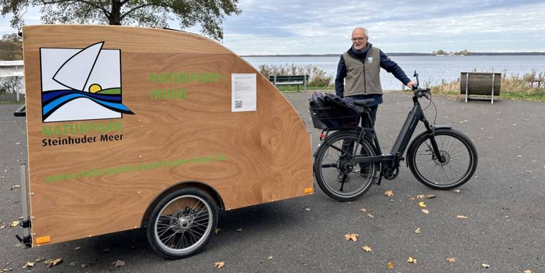 Mann mit einem Gespann aus E-Bike und Fahrrad-Wohn-Anh&auml;nger