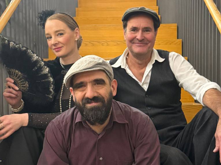 Eine Frau mit zurückgebundenem Haar und Fächer und zwei Männer sitzen auf einer Treppe.