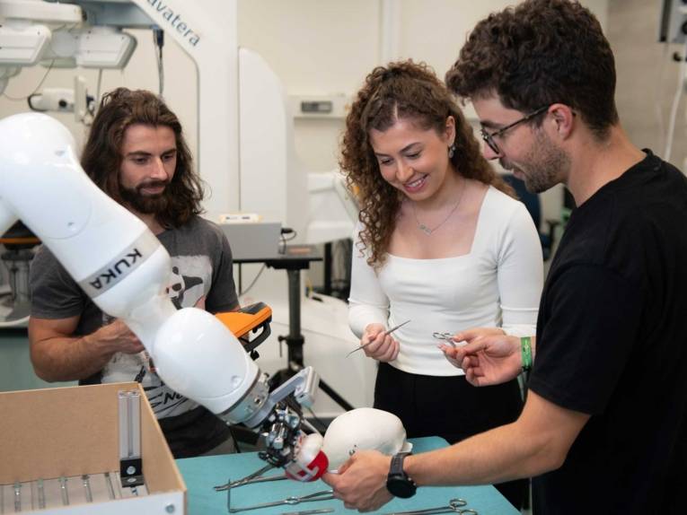 Zwei Männer und eine Frau mit Roboterarm.