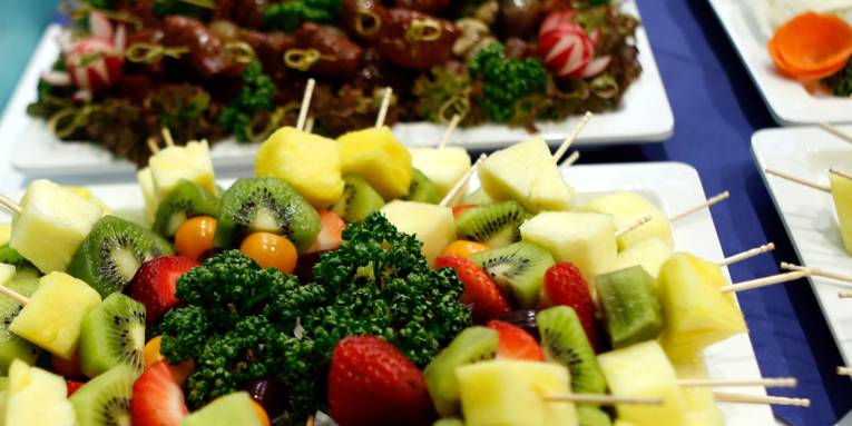 Spieße mit Obst, Käse und anderen Lebensmitteln liegen auf verschiedenen Tellern und Platten.