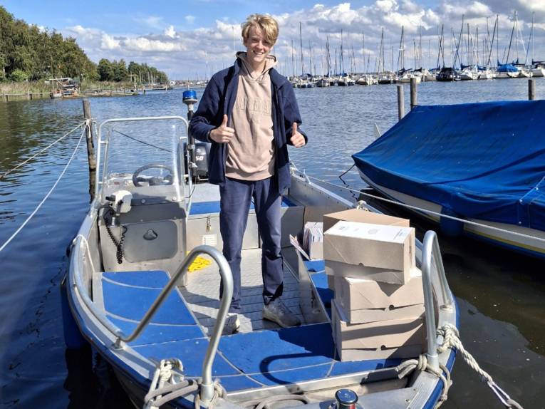 Ein Mann steht auf einem Boot, auf dem Boot stapeln sich Kartons.