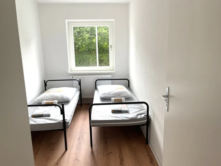 Blick in einen schmalen Raum, links und rechts ein Bett, in der Mitte ein Fenster.