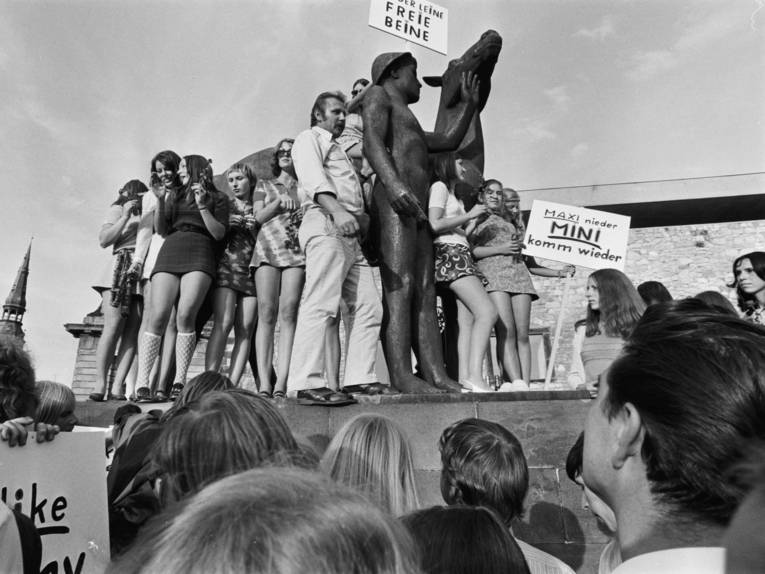 Das Bild ist eine Schwarz-Weiß-Fotografie von Joachim Giesel, auf dem eine Protestaktion zum Tragen von Mini-Röcken an der Leine in Hannover aus dem Jahr 1970 zu sehen ist.