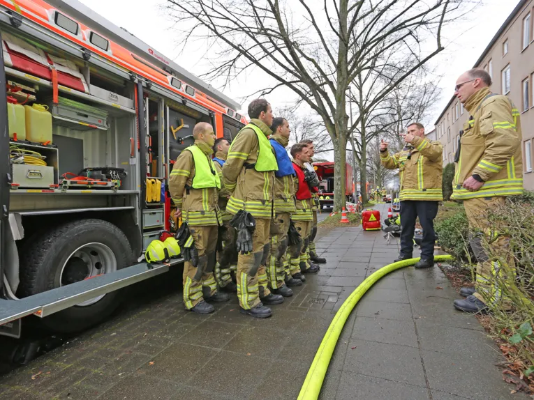 Auszubildende Feuerwehrmänner stehen vor einem Fahrzeug