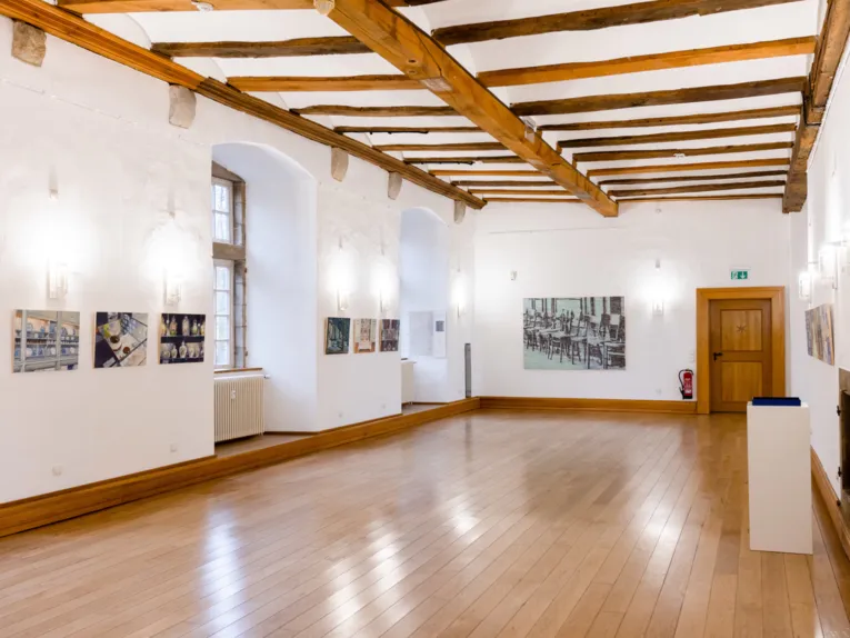 Blick in einen historischen Saal. An den W&auml;nden h&auml;ngen Bilder, der Boden ist &uuml;berwiegend frei.
