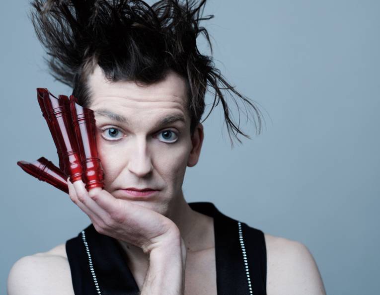 Mann mit wild verstrubbelten Haaren stützt das Kinn in die rechte Hand, an jedem Finger steckt das Oberteil einer Blockflöte.