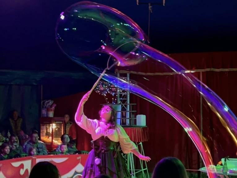 Frau, die in einer Zirkusmanege eine Riesenseifenblase erzeugt.