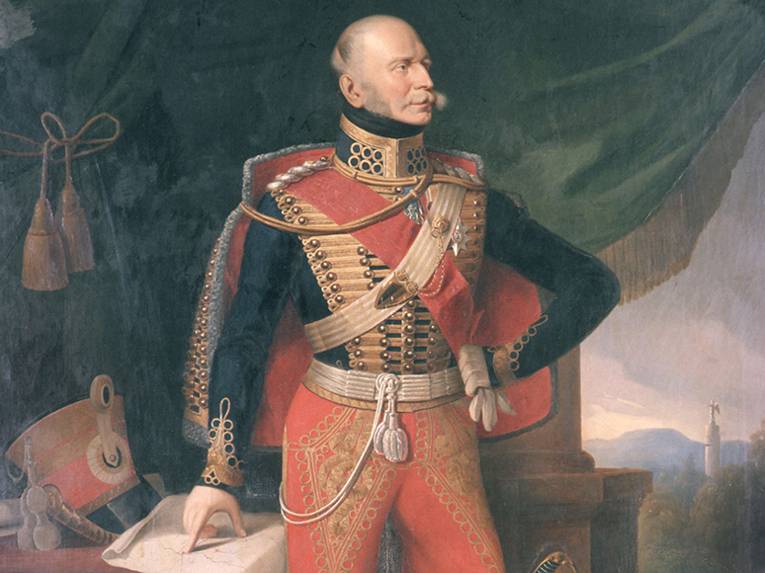 König Ernst August von Hannover, Öl/Leinwand, Edmund Koken 1842; gemalt nach einem Bildnis von Franz Krüger, Gemäldeausschnitt. In der Bildmitte Ganzfigur des Königs in Husarenuniform (rote Hose, dunkelblauer, goldtressenbesetzter Rock, rot gefütterter Dolman) mit rotem Schulterband und Bruststern des St. Georgs-Ordens, den Kopf nach links gewandt, die linke behandschuhte Hand mit dem anderen Handschuh darin in die Hüfte gestemmt, hinter dem linken Bein der Schleppsäbel, rechte Hand auf eine Karte des Königsreichs Hannover weisend, die auf einem mit roter Decke behängten Tisch liegt; daneben der Tschako des Königs und eine Papierrolle