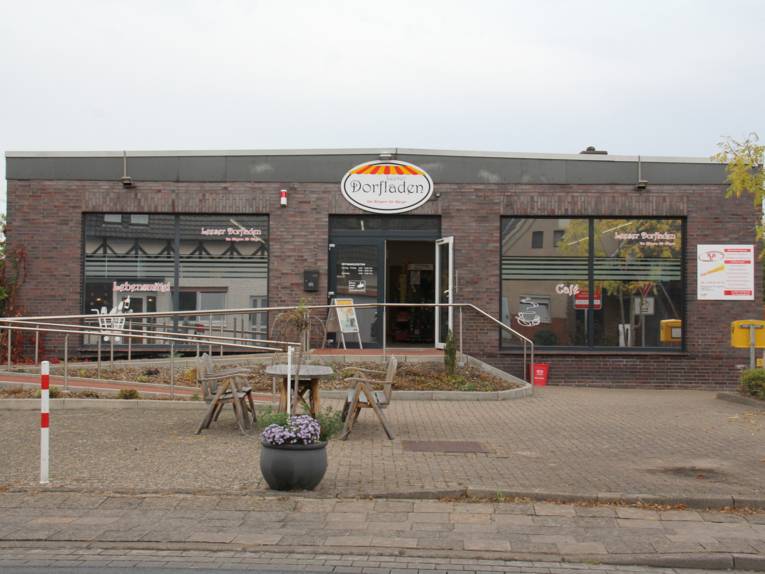 Geb&auml;ude mit Schild Dorfladen, davor eine Sitzgruppe aus Holz