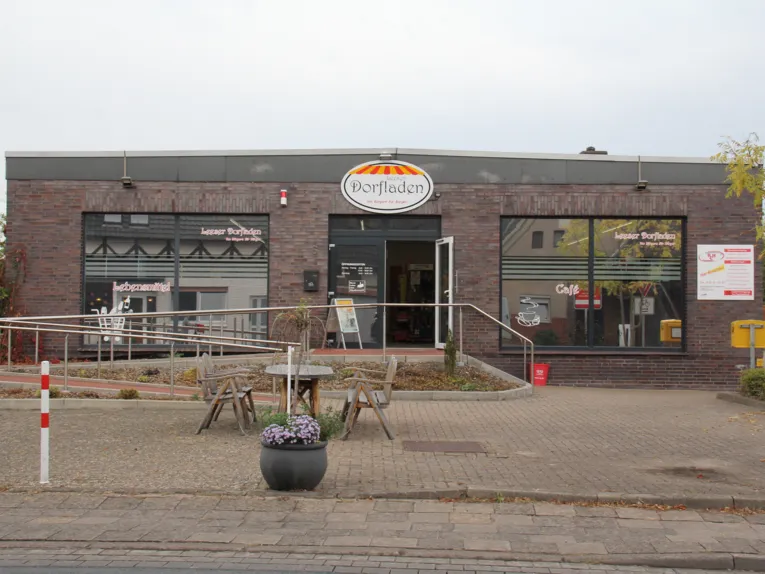 Gebäude mit Schild Dorfladen, davor eine Sitzgruppe aus Holz