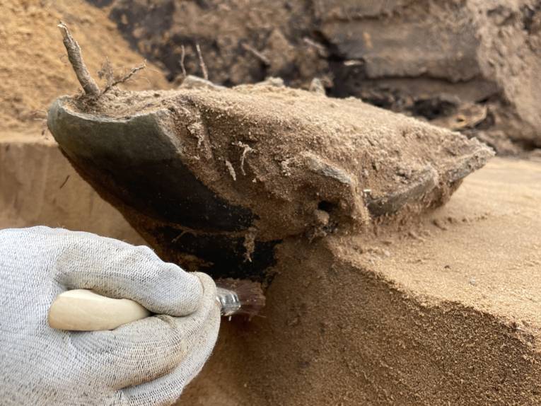 Bruchstück einer Urne aus der Bronzezeit. Mit einem Pinsel wird das Bruchstück freigelegt