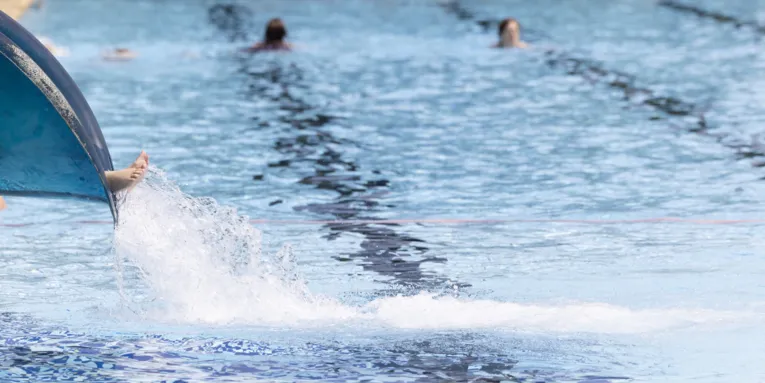 Füsse einer Person, die gerade auf einer Aussenrutsche im Freibad an Übergang ins Wasser angekommen ist