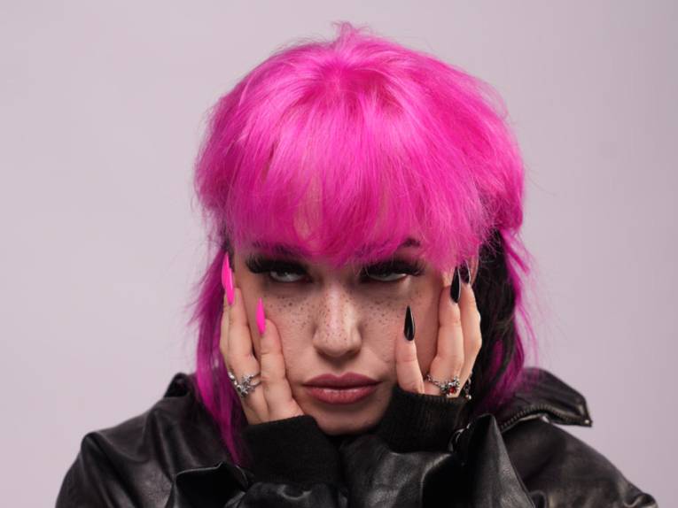 Die Sängerin mit pinken Haaren hält die Hände an ihr Gesicht.