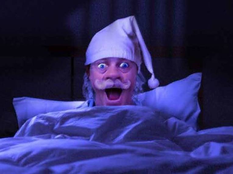 Mann mit großem Schnauzbart und Nachtmütze in einem Bett