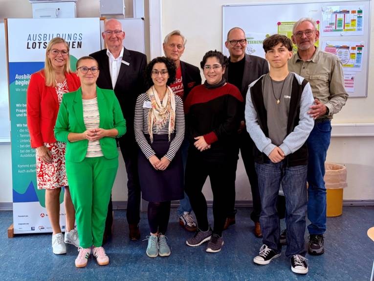 Auf dem Foto stehen mehrere Menschen, darunter Erwachsene und Schüler*innen, die in die Kamera schauen.