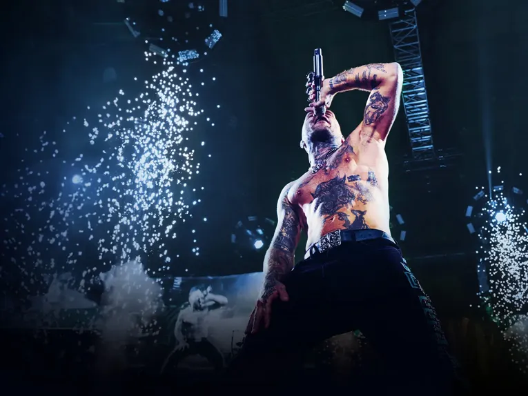 Der Rapper Kontra K steht oberkörperfrei mit Mikro auf einer Bühne umgeben von Pyrotechnik