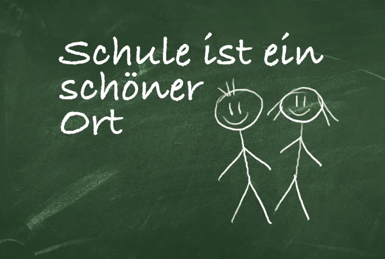 Tafelbild mit zwei lächelnden Strichpersonen und der Überschrift "Schule ist ein schöner Ort"