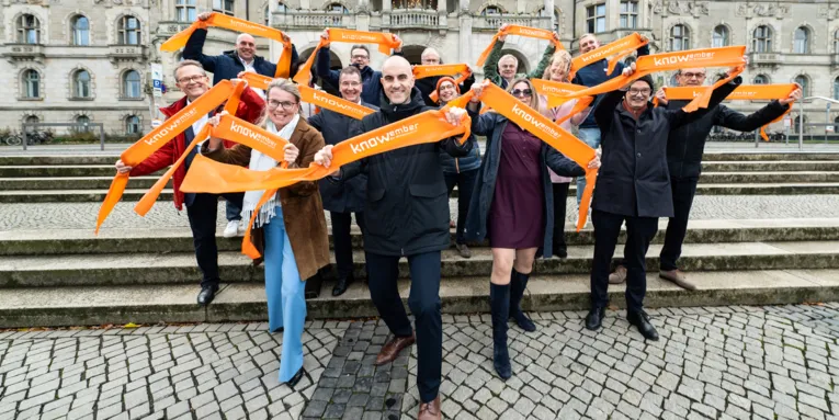 Männer und Frauen auf der Freitreppe vor dem Neuen Rathaus halten Bänder mit dem Schriftzug "knowember" in die Höhe.
