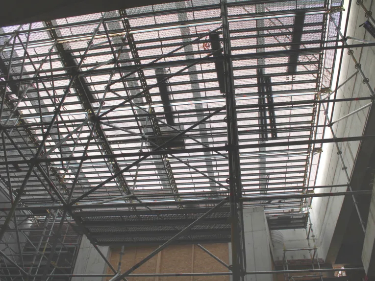 Hinter einem Bauger&uuml;st oben eine Stahlkonstruktion mit Lichteinfall, rechts ein St&uuml;ck Betonwand.