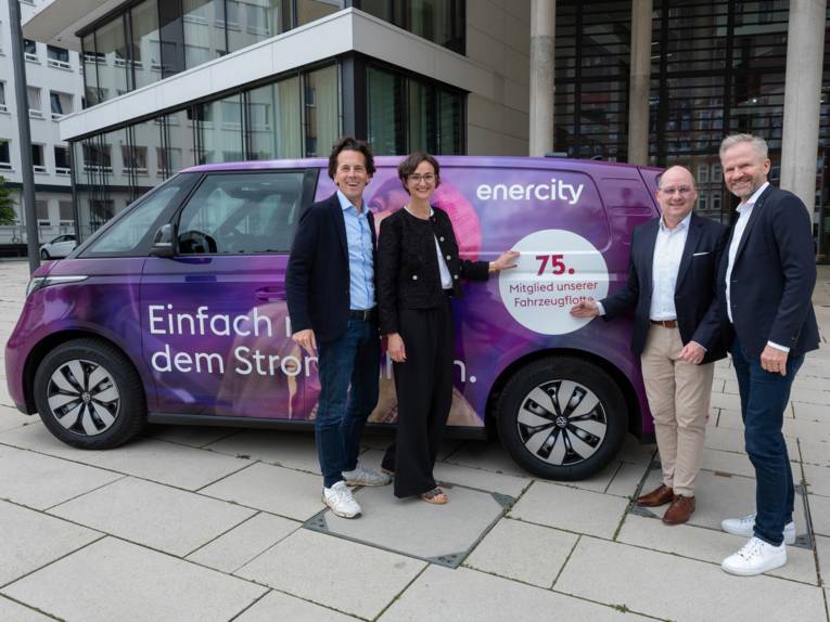 Drei Männer und eine Frau stehen vor einem E-Auto.