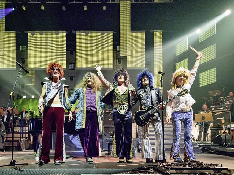 Fünf bunt kostümierte Menschen stehen mit ihren Instrumenten auf der Bühne.