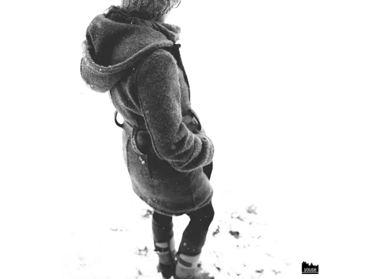 Schwarz-Weiß-Foto einer Person in einem Wollwalkmantel im Schnee.