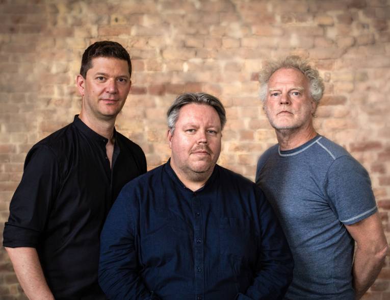 Drei Männer vor einer alten Backsteinwand