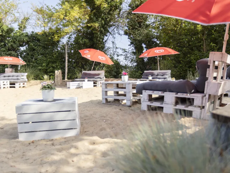 Gro&szlig;e Sandfl&auml;che mit Sitzgelegenheiten aus Palletten mit Kissen, Pallettentische mit Blumen