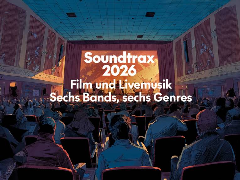 ein Saal mit Bühne und Leinwand. Auf der Bühne vor der Leinwand eine Band.