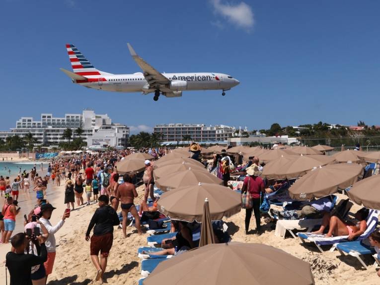 Ein Flugzeug fliegt tief &uuml;ber einem vollen Strand