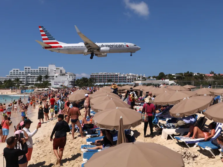 Ein Flugzeug fliegt tief &uuml;ber einem vollen Strand